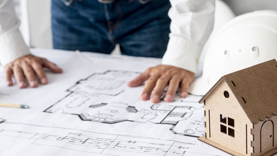 Plans d'une maison, maquette et casque de chantier sur une table de travail
